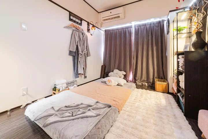 完全個室の施術室。床に敷いたマットの上にタオルと枕が用意され、壁のハンガーには着替え用のガウンが掛かっている