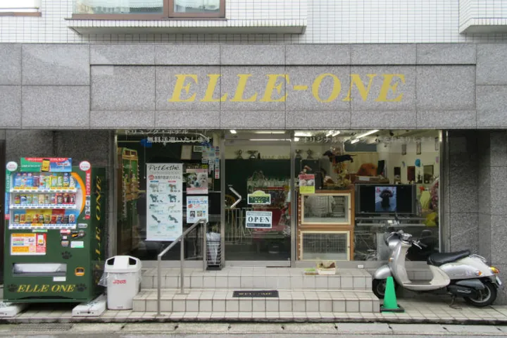 「ELLE-ONE」の看板を掲げた路面店の外観。ガラス張りで店内の様子が通りから見え、入口の左手に自動販売機、右手にスクーターが停まっている